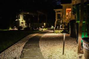 dark sidewalk being lit up by landscape lighting fixtures gravel alongside