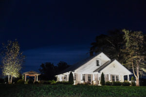wide shot of white home with double vaulted roofing at night beautiful green grass inground lighting