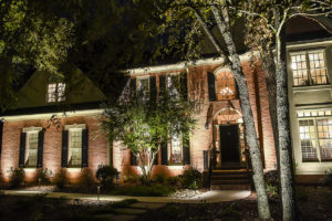 view of brick home at night with inground lighting around walkway to front porch