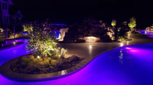 night view of backyard pool with hues of purple pink and blue island of plants in middle